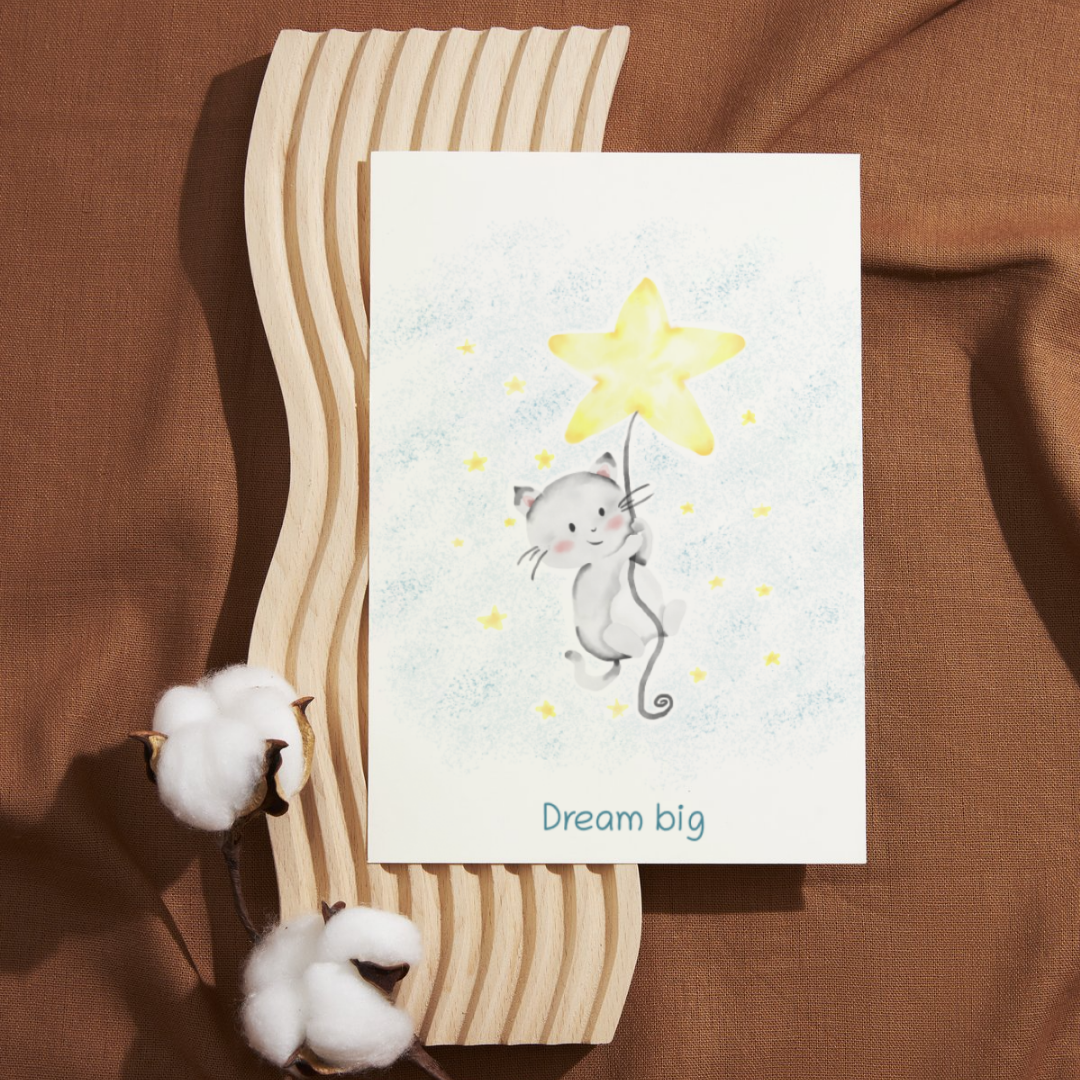 Card with a cat holding a star and 'Dream big' text on a brown fabric background